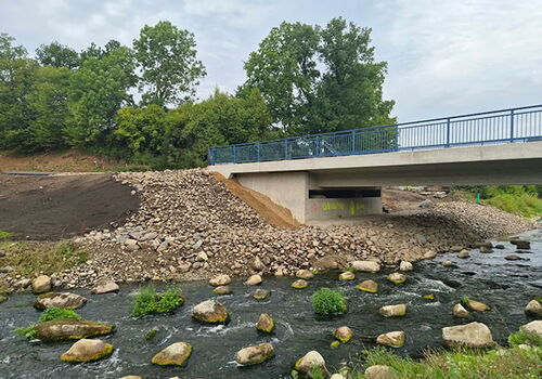 Brücke über Bach mit Felsen und Pflanzen im Wasser.