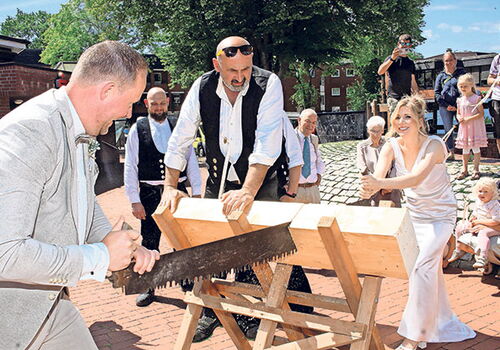Brautpaar sägt gemeinsam ein Holzstück durch.