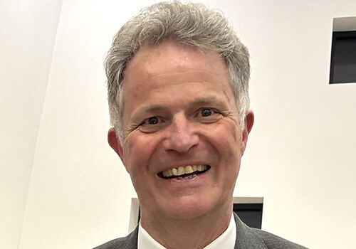 Mann in Anzug hält Geschenkkorb, lächelt freundlich.