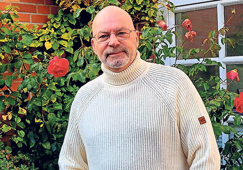 Mann in weißem Pullover vor Rosen im Garten
