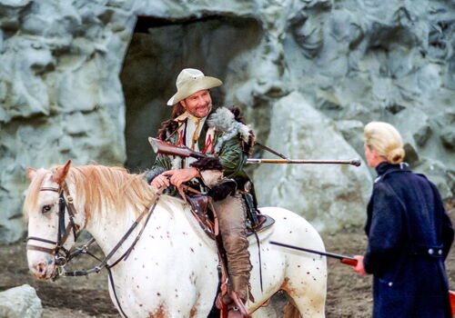 Mann auf Pferd in historischem Kostüm vor einer Höhle.
