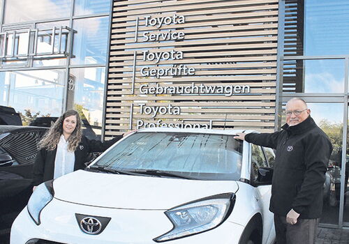 Zwei Personen stehen neben einem weißen Toyota vor einem Autohaus.