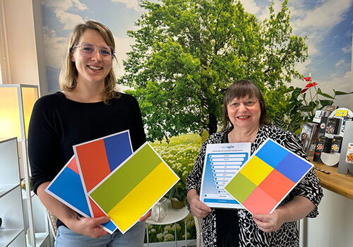 Zwei Frauen halten bunte Karten und Diagramm vor Baum.
