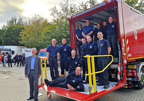 Gruppe von Feuerwehrleuten posiert auf Einsatzfahrzeug.