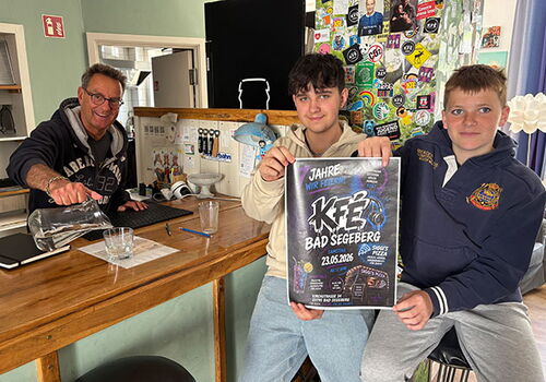 Drei Personen in einem Café mit Festivalposter.