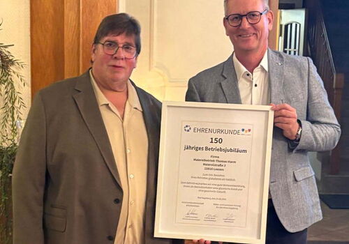 Zwei Männer halten eine Ehrenurkunde für 150 Jahre Jubiläum.