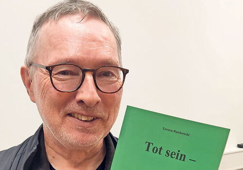 Mann hält ein grünes Buch mit dem Titel 'Tot sein'.