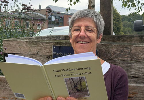 Frau liest Buch auf einer Bank im Freien.