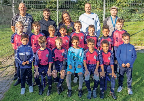Kinder-Fußballteam posiert mit Trainern im Freien.