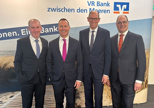Vier Männer in Anzügen vor VR Bank Banner.