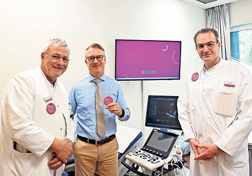 Drei Ärzte in einem Untersuchungsraum mit medizinischem Gerät.
