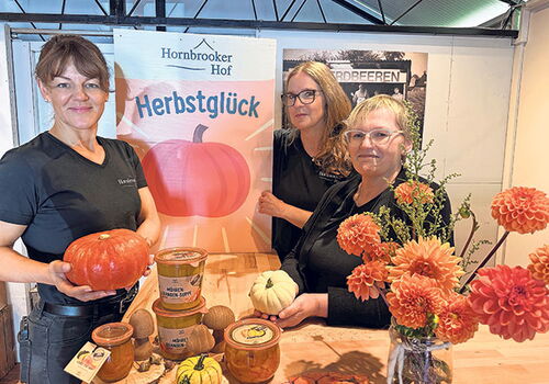 Drei Frauen präsentieren Kürbisprodukte auf einem Herbstmarkt.