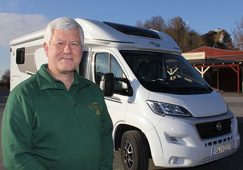 Mann steht vor weißem Wohnmobil bei Sonnenschein.