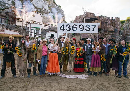 Gruppe posiert mit Sonnenblumen vor Felsenbühne.