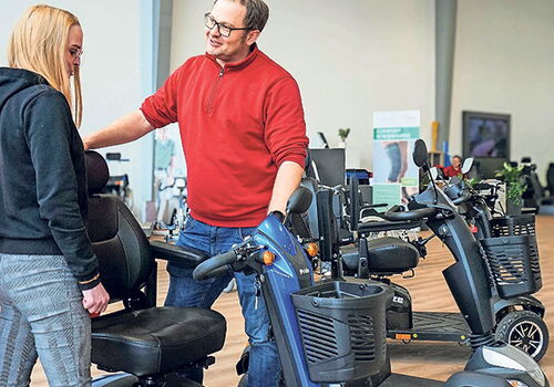 Mann zeigt Frau einen Mobilitätsscooter im Geschäft.