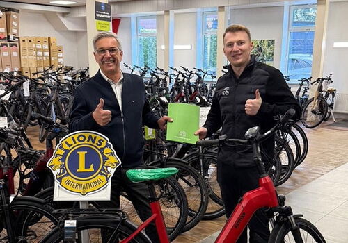 Zwei Männer stehen mit Daumen hoch neben einem roten Fahrrad.