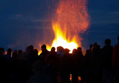 Menschenmenge versammelt sich um ein großes Lagerfeuer bei Nacht.