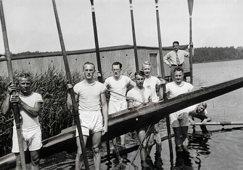 Ruderteam posiert mit Boot am Seeufer.