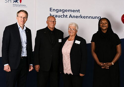 Vier Personen vor einem Schild mit Text.
