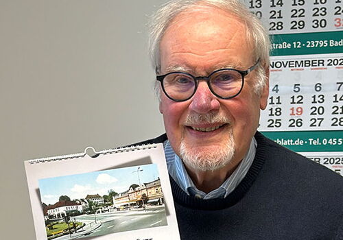 Mann hält Kalender für 2026 mit historischem Foto.