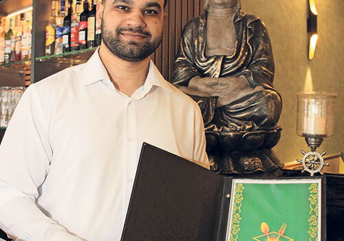 Mann zeigt Speisekarte in einem Restaurant mit Buddha-Statue.