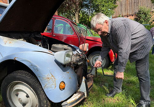 Mann startet blauen Oldtimer mit Kurbel bei Sonnenschein.