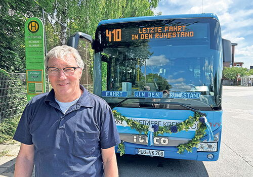 Busfahrer vor dekoriertem Bus mit Ziel: Ruhestand.
