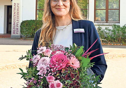 Frau mit Blumenstrauß vor einem Gebäude lächelt in die Kamera.