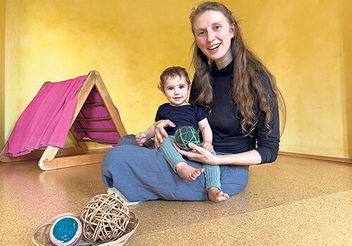 Frau mit kleinem Kind spielt mit Bällen auf dem Boden.
