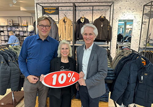 Drei Personen halten ein Schild mit 10% in einem Bekleidungsgeschäft.