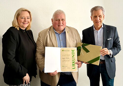 Drei Personen mit einer Urkunde und Geschenkbox.