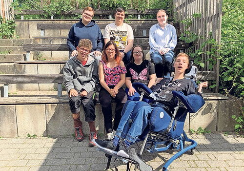 Gruppe von sieben Personen sitzt auf einer Tribüne im Freien.
