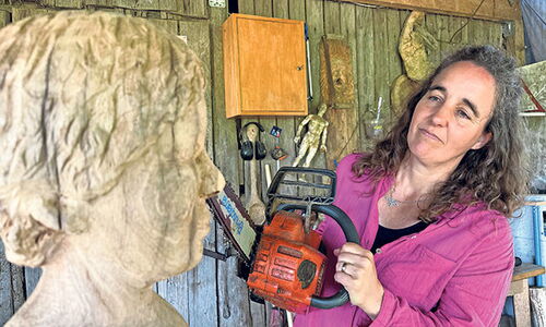 Frau schnitzt Holzskulptur mit Motorsäge in Werkstatt.