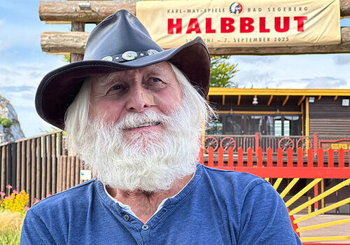 Mann mit Cowboyhut vor Halblut-Plakat.