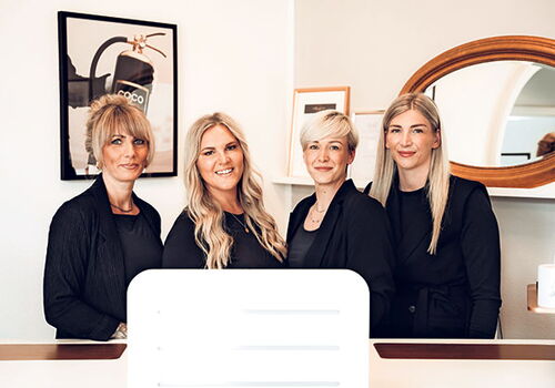 Vier Frauen stehen lächelnd hinter einem Empfangstresen.
