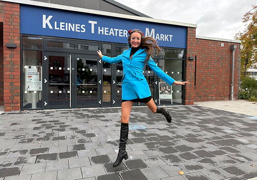 Frau springt vor dem Kleinen Theater Markt.