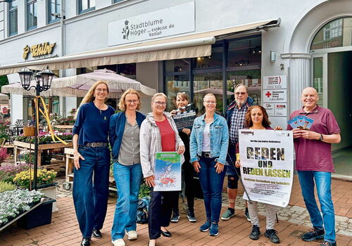Gruppe von Menschen vor einem Blumenladen mit Plakaten.