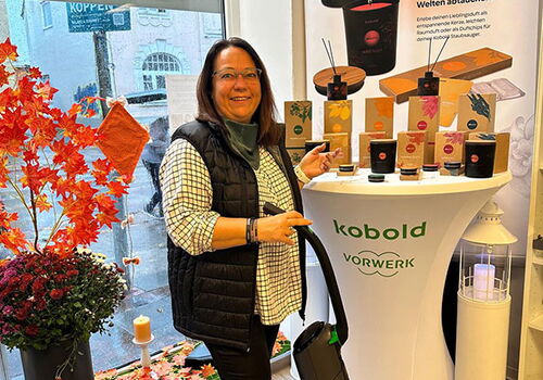 Frau mit Staubsauger neben Duftproduktpräsentation im Laden.