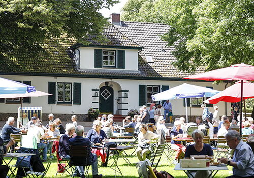 Menschen sitzen an Tischen im Freien vor einem Haus.