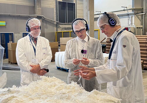 Drei Männer in Laboranzügen untersuchen Material im Labor.