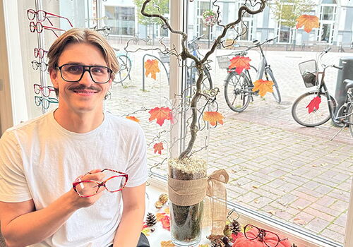 Mann mit Brille sitzt lächelnd in einem herbstlichen Fensterdisplay.