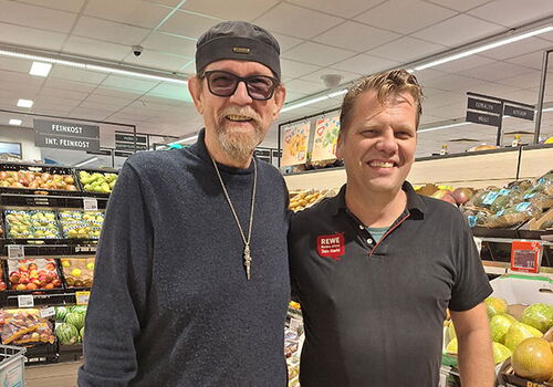 Zwei Männer in einem Supermarkt lächeln für ein Foto.
