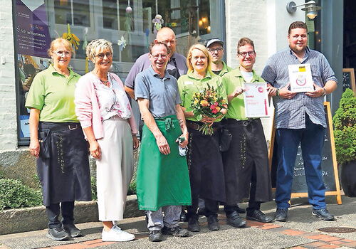 Gruppe von Menschen vor einem Café mit Auszeichnungen und Blumen.
