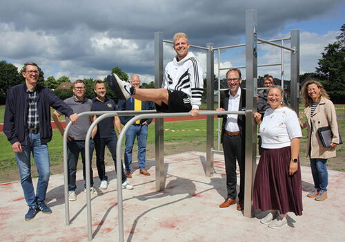 Gruppe posiert an Außensportanlage bei bewölktem Himmel.