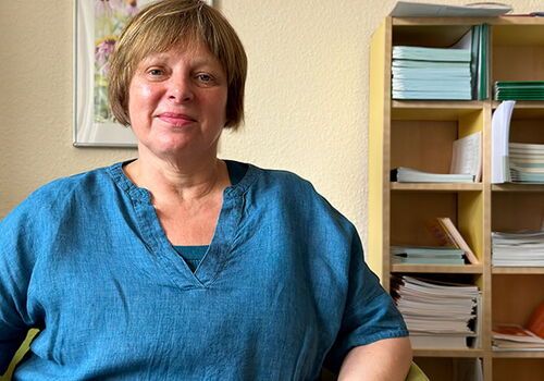 Frau in blauem Hemd sitzt vor einem Regal mit Büchern.