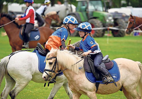 Zwei Kinder spielen Polo auf Ponys auf einem Spielfeld.
