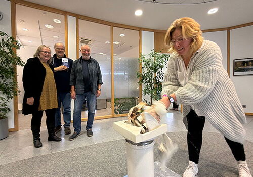 Frau zerschlägt symbolisch Porzellan vor drei Beobachtern im Büro.