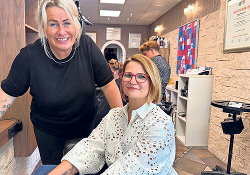 Zwei Frauen im Friseursalon, eine sitzt, eine steht.