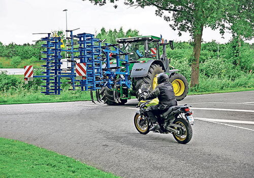 Traktor mit Anbaugerät, Motorrad auf Landstraße.