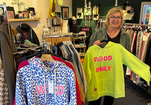 Frau in Boutique hält gelben Hoodie mit Aufschrift.